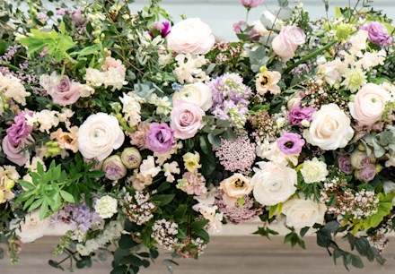 Large floral display filled with fresh cut flowers in shades of light pink and white, surrounded by seasonal foliage