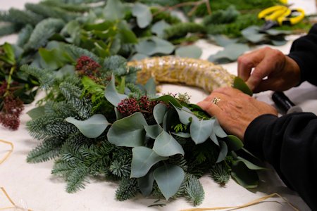 image of someones hands adding foliage to a straw wreath and securing in place